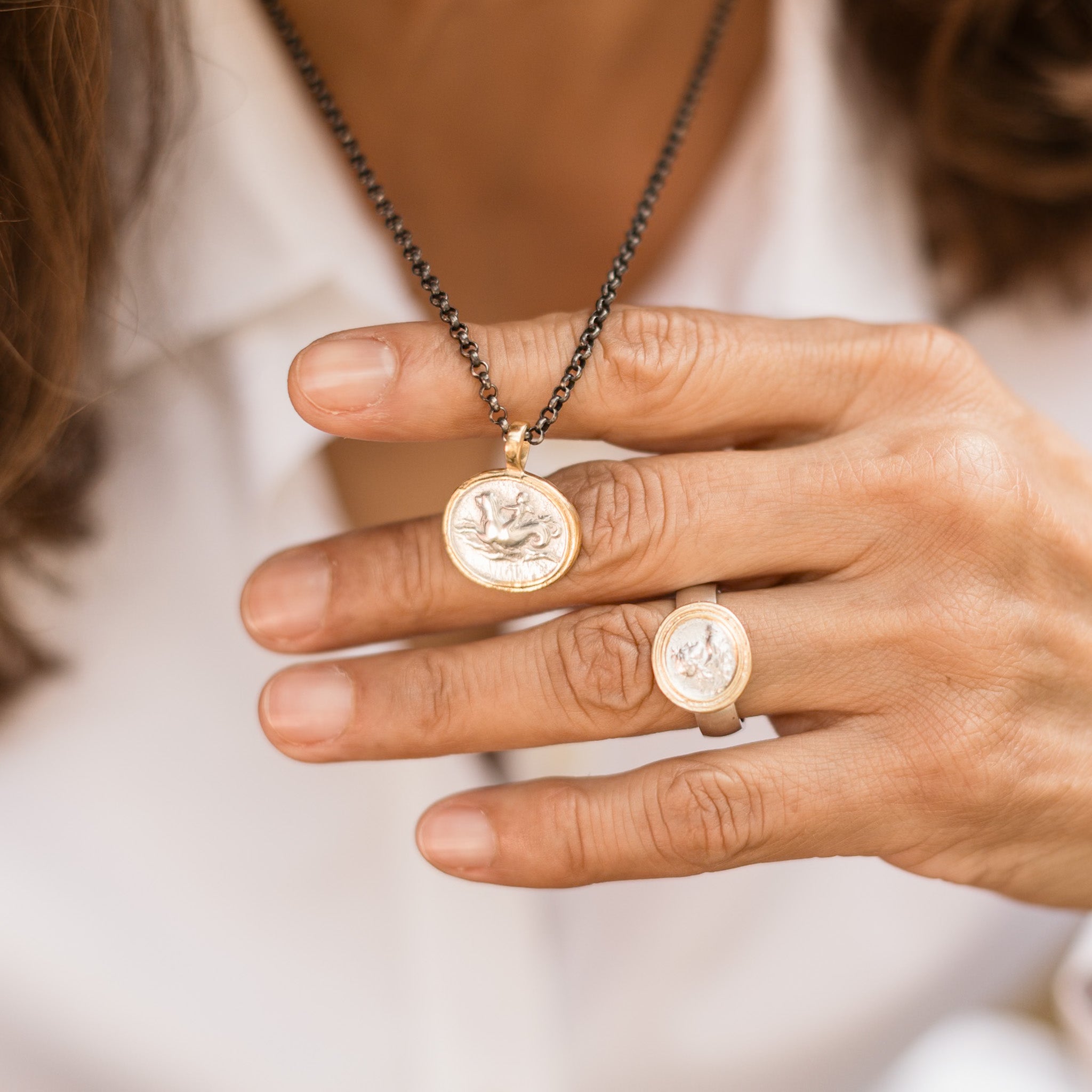 Nahaufnahme von Kette Marina mit Münze Wellenreiter Motiv, und dem Ring Apollon, dem Gott der Kunst und des Lichts. Beide Stücke aus Sterling Silber, bicolor vergoldet. True Nuggets
